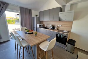 Une cuisine moderne avec un coin repas, comprenant une table en bois, des chaises blanches, un saladier de fruits et une vue sur l’extérieur.