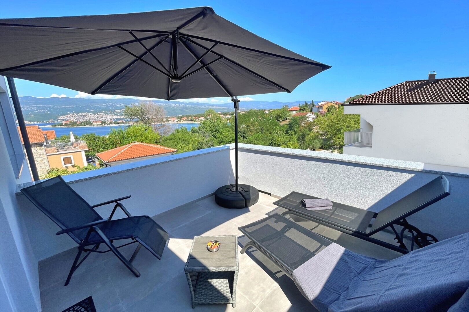 A balcony with a black umbrella, a chair, a table, and a sofa.
