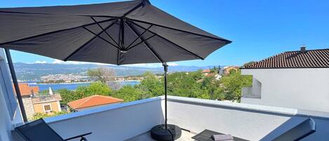 Un balcon avec un parasol noir, une chaise, une table et un canapé.
