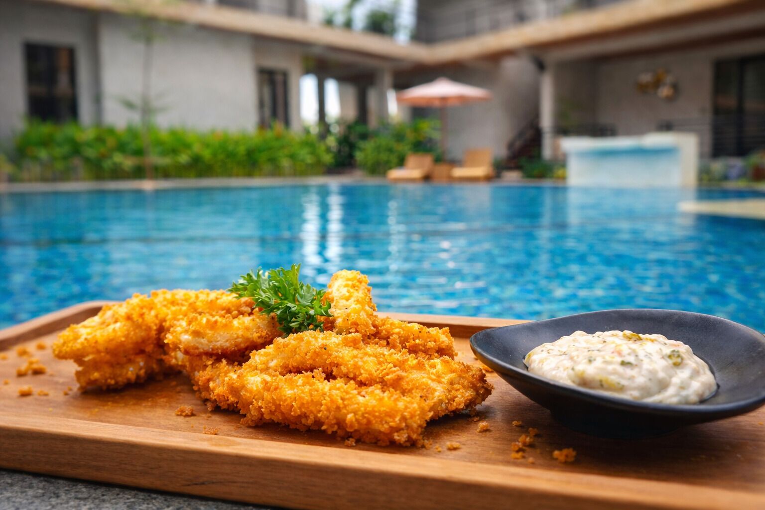 Vista de la piscina con una tabla de alitas de pollo rebozadas y un bol de salsa.