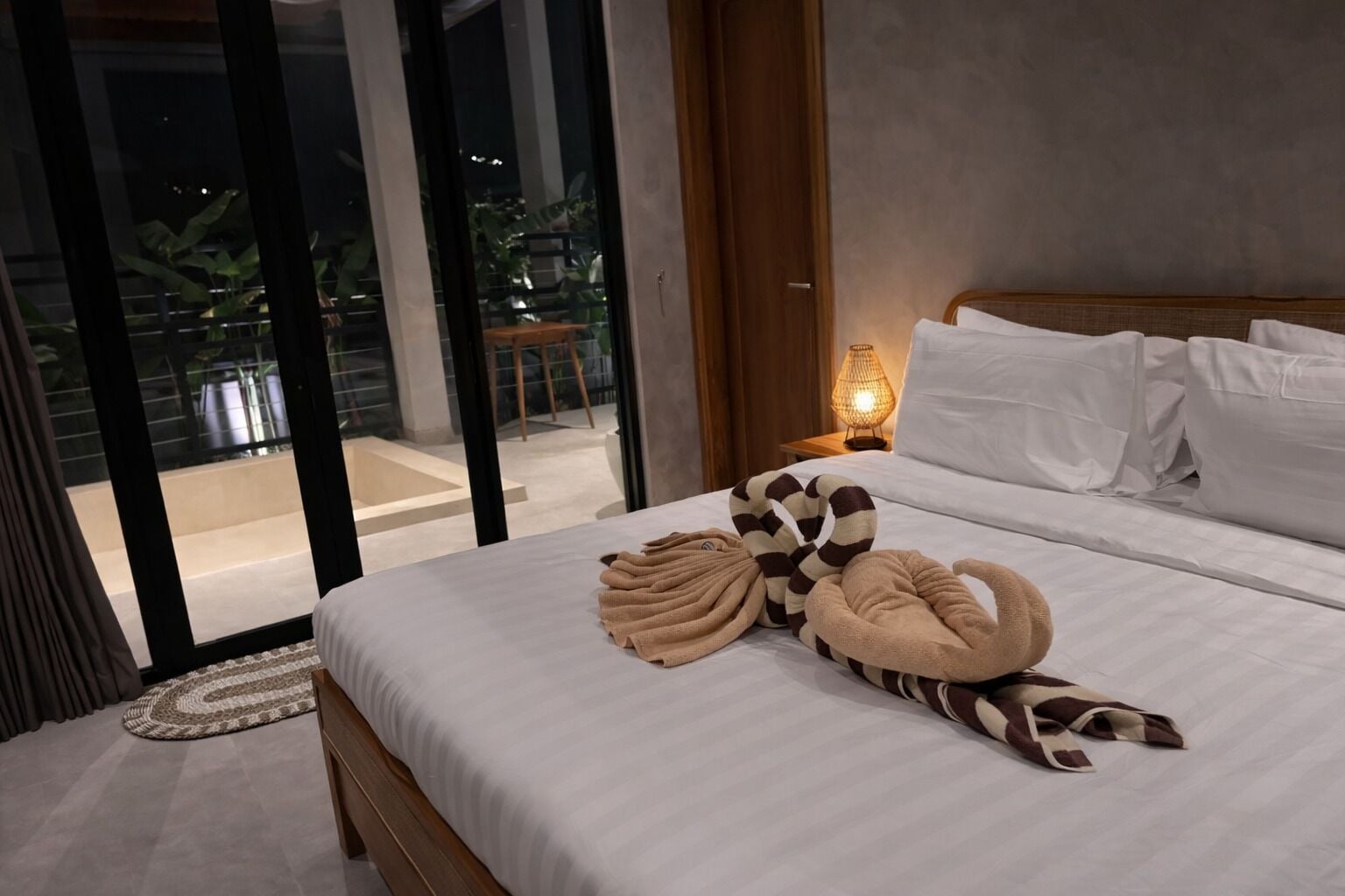 Une chambre d’hôtel moderne avec un grand lit, une vue sur l’extérieur et une table de chevet avec une lampe.