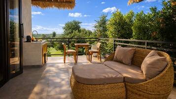 Un balcon aménagé avec un canapé en osier, deux fauteuils, une petite table et un coin bar.
