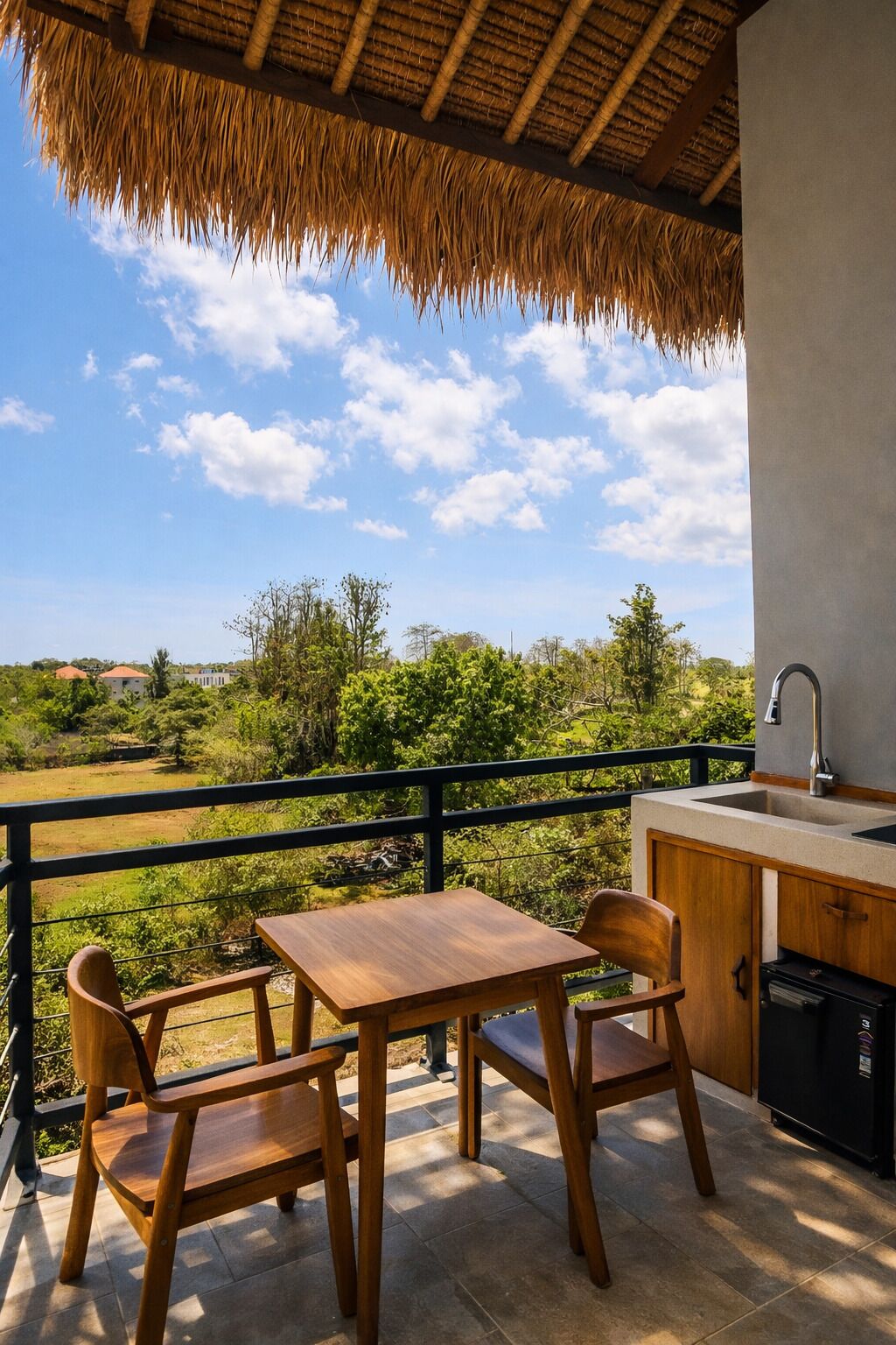 A balcony with a wooden table and chairs, a sink, and a view of a green landscape.