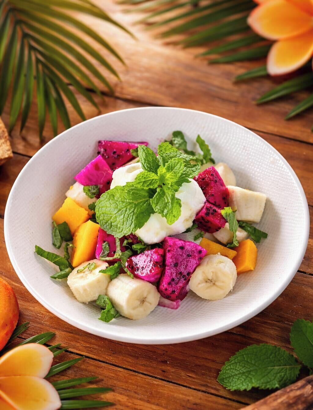 A white plate with a fruit salad including dragon fruit, mango, banana, and mint leaves.