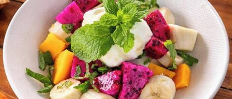 A white plate with a fruit salad including dragon fruit, mango, banana, and mint leaves.