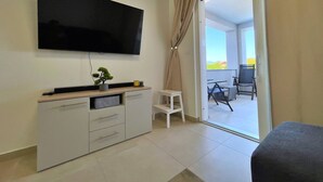 Een moderne woonkamer met een flatscreen televisie, een klein wit tafeltje en een bank.