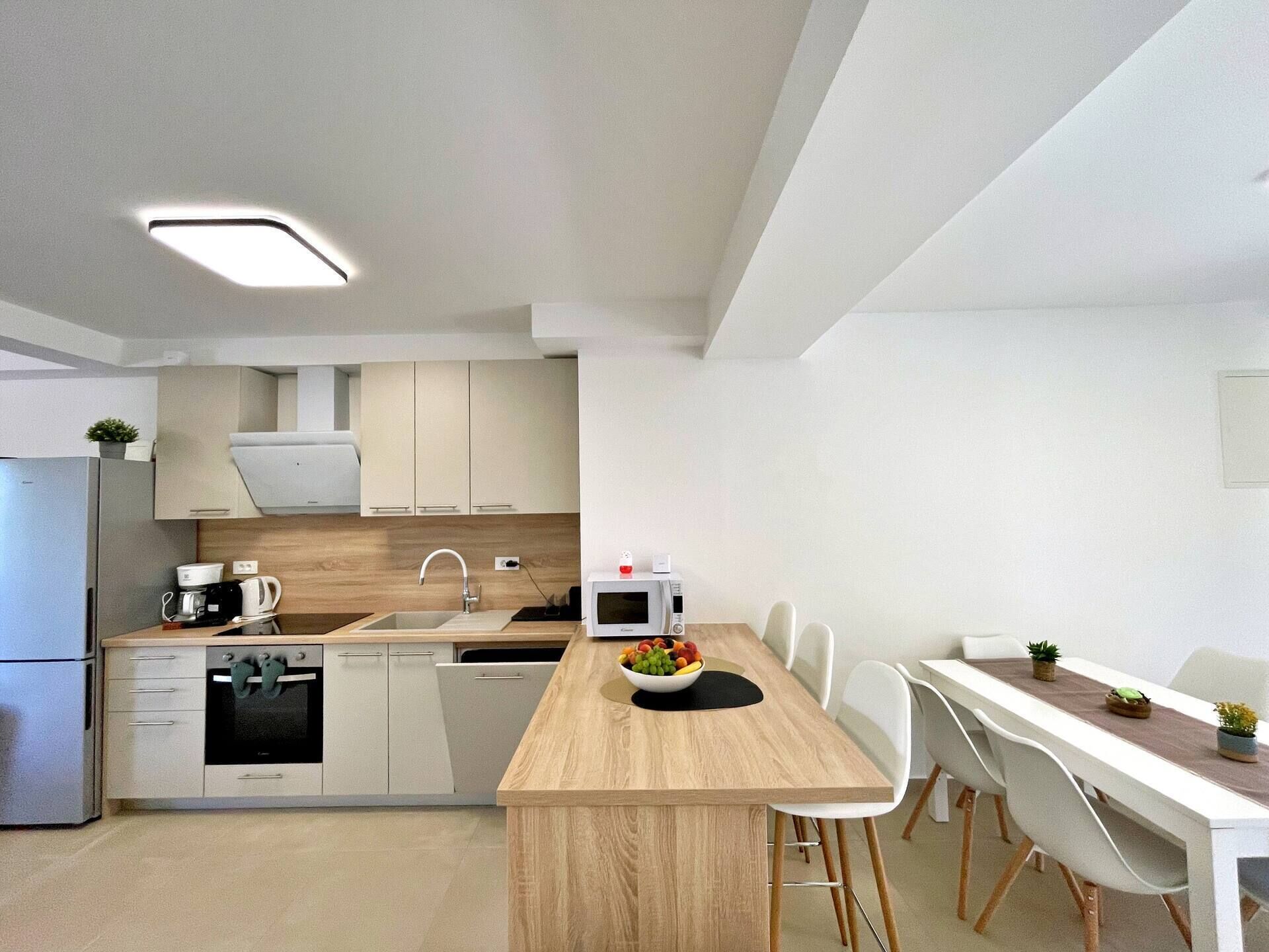 A modern kitchen with a central island, white cabinetry, and a dining area with a long table and chairs.