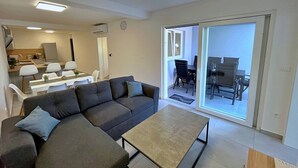 A modern living room with a grey sectional sofa, a small coffee table, and a dining area with a white table and chairs. - Luxury Apartment Bonum - modern, luxury, private swimming pool, terrace, air conditioning, private parking, washing machine (Šilo)