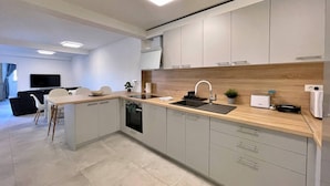 A modern kitchen with a built-in dishwasher, a sink, and a countertop. There is a dining area with a table and chairs. - Luxury Apartment Bonum - modern, luxury, private swimming pool, terrace, air conditioning, private parking, washing machine (Šilo)