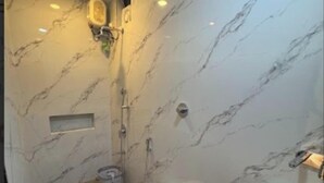 A bathroom with a marble wall, a toilet, a bidet, a sink, and a shower. - Hotel Tulsi Inn (Ellora)