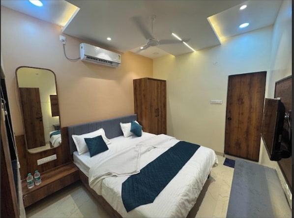 Una camera da letto con un letto, un ventilatore a soffitto, un condizionatore d'aria, armadi in legno, uno specchio e una porta.
