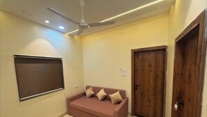 A room with a ceiling fan, a window with blinds, a pink sofa with cushions, and a wooden door. - Hotel Tulsi Inn (Ellora)