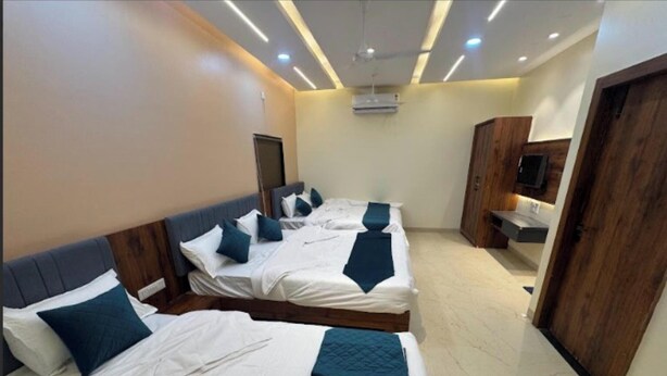 A hotel room with three beds, a wooden wardrobe, a TV, and a ceiling fan. - Hotel Tulsi Inn (Ellora)