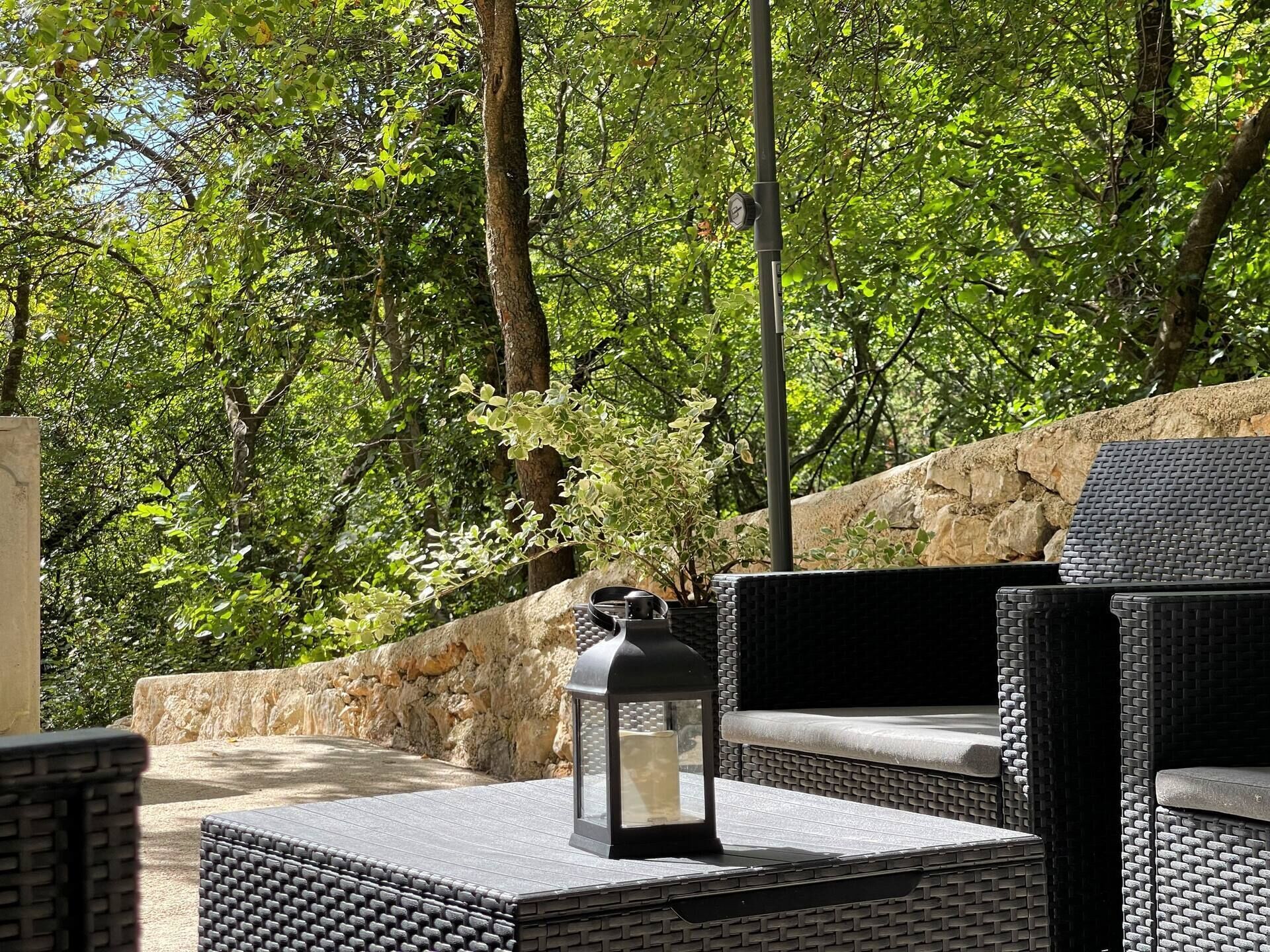 An outdoor seating area with wicker furniture, a stone wall, and a lantern.