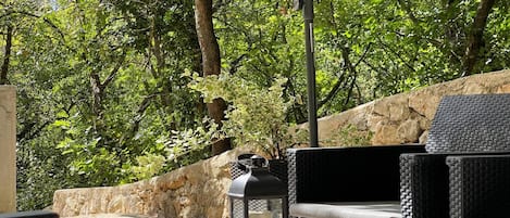 An outdoor seating area with wicker furniture, a stone wall, and a lantern.