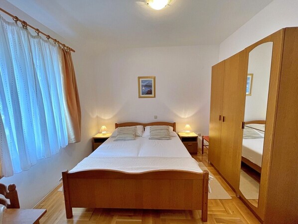 A bedroom with a wooden bed, two bedside tables with lamps, a large wardrobe, and a window with curtains.
