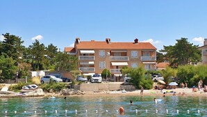 A coastal building with multiple balconies, a swimming area with people, and parked cars.