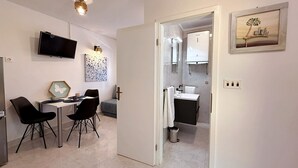Une chambre d’hôtel moderne dotée d’un coin repas, d’une télévision, d’un tableau et d’une salle de bain avec un lavabo et un miroir.