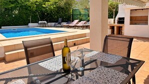 Un espace aménagé au bord de la piscine, avec une table, des chaises et une bouteille de vin.