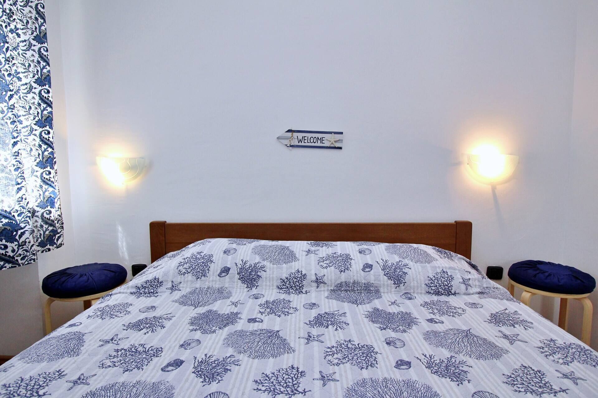 Quarto com cama, duas mesas de cabeceira, uma placa na parede e duas luminárias de parede.