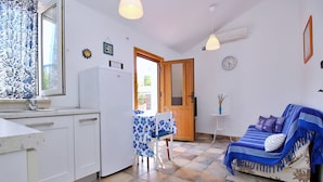 A compact kitchen with a refrigerator, a dining table with a blue floral tablecloth, and a blue sofa with a patterned throw. - Apartment Bujas - 160 m from the sea, free parking, BBQ, ground floor (Šilo)