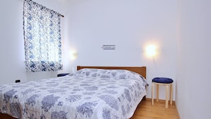 A bedroom with a bed, two nightstands, a wall-mounted light, and a window with patterned curtains. - Apartment Bujas - 160 m from the sea, free parking, BBQ, ground floor (Šilo)
