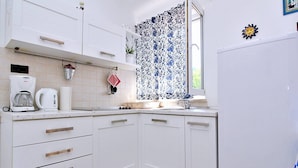 A compact kitchen with white cabinets, a Bosch coffee maker, a kettle, and a window with patterned curtains. - Apartment Bujas - 160 m from the sea, free parking, BBQ, ground floor (Šilo)
