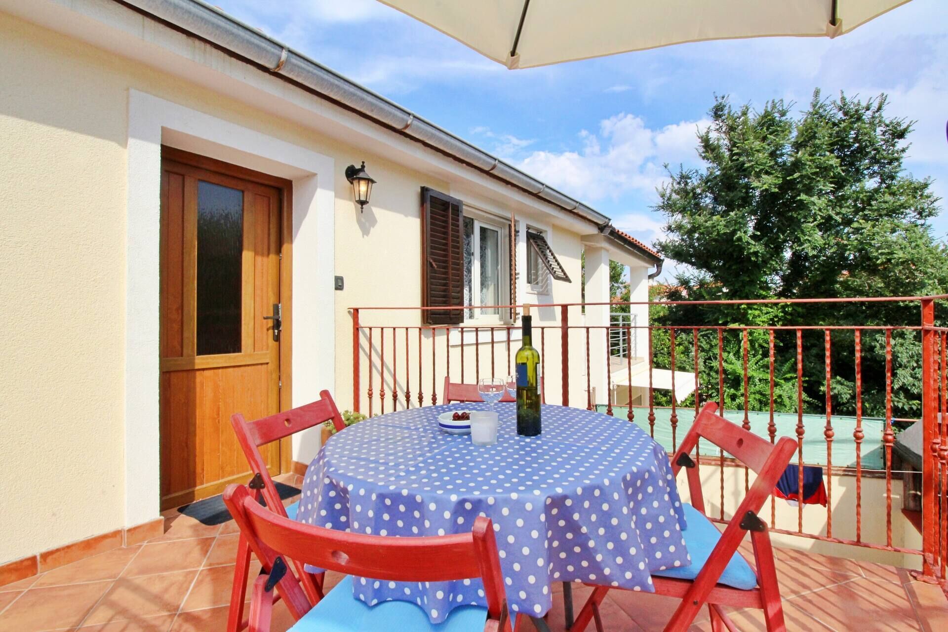 A patio with a round table covered by a blue polka dot tablecloth, surrounded by red chairs.
