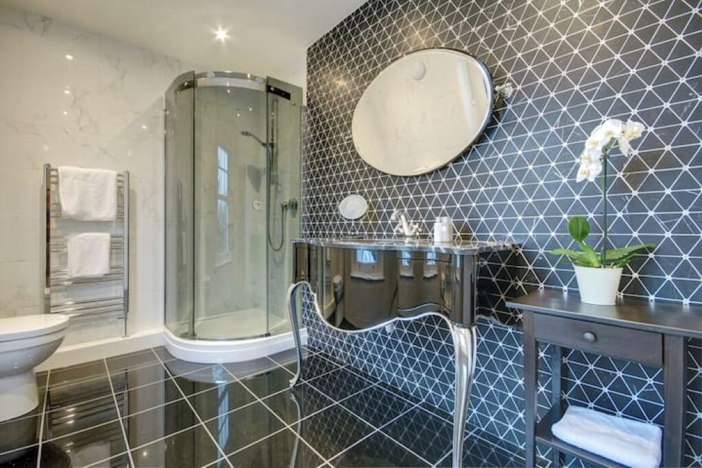 Une salle de bain moderne avec une douche à parois de verre, un miroir rond et un mur recouvert de carreaux.