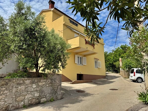 Un bâtiment jaune avec un mur en pierre et une voiture blanche garée devant.