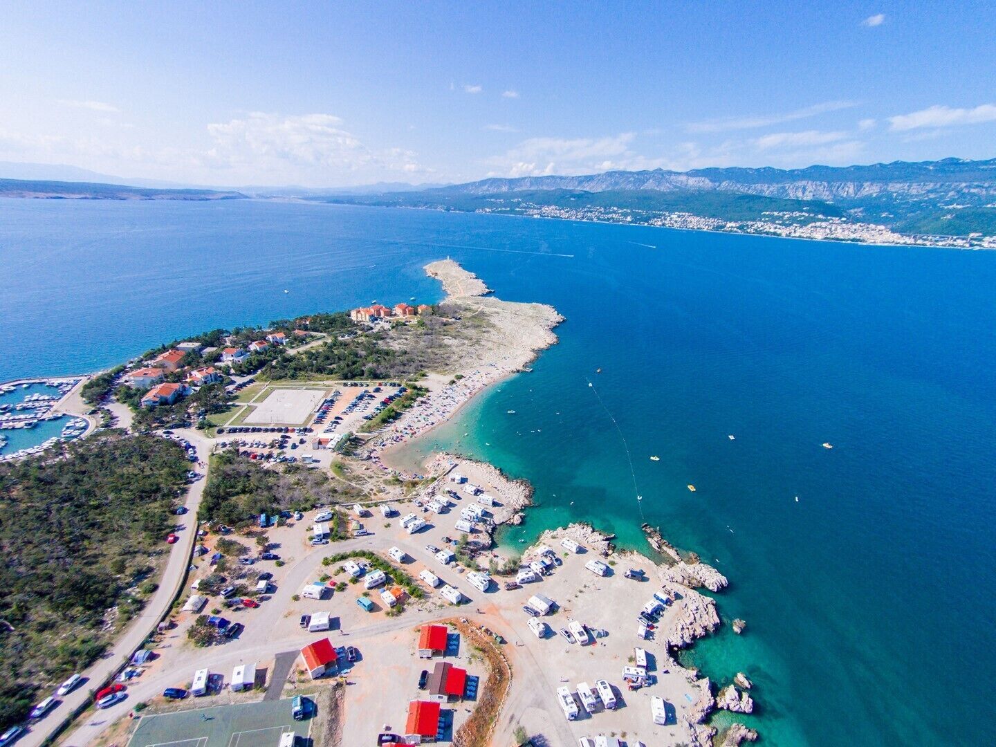 Vue aérienne d’une zone côtière comprenant un port de plaisance, un espace de stationnement pour les véhicules de loisirs et une plage.