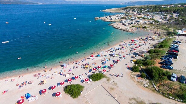 An aerial view of a beach with numerous umbrellas and people, a clear blue sea, and a parking area with cars. - Apartment Car - 90 m from the sea, private terrace, parking, BBQ (Šilo)
