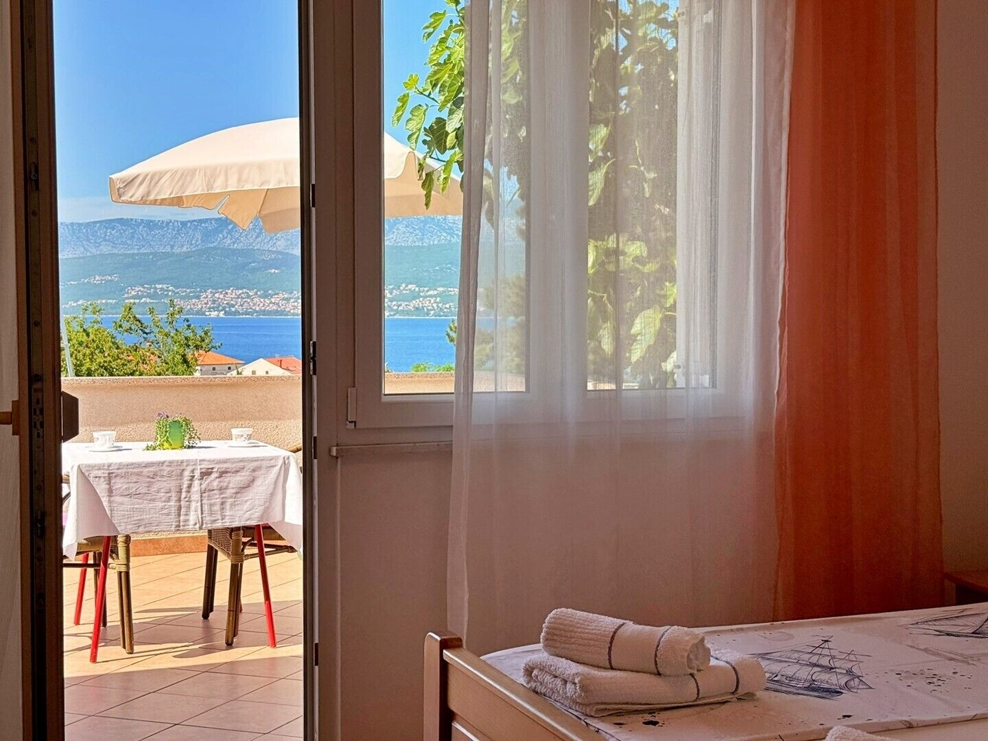 Una habitación con vista al mar, una mesa con sillas y una cama con toalla.