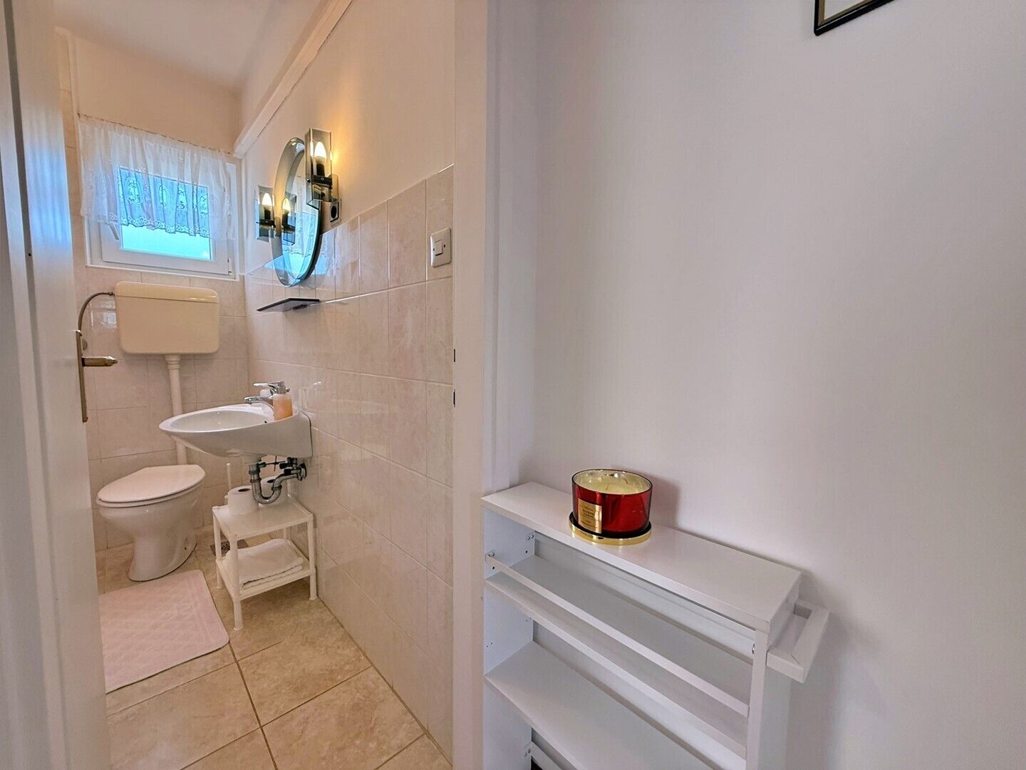 A bathroom with a toilet, sink, and a shelf with a red container.