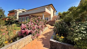 A two-story house with a balcony, a garden with flowering plants, and a clear blue sky. - Apartment Dragica - sea view, 350 m from sea, balcony, free parking, BBQ (Šilo)