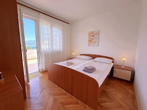 Un dormitorio con una cama de madera, dos lámparas de noche, un ventanal con cortinas traslúcidas y un cuadro en la pared.