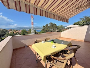 Una terraza con una mesa y sillas, vista al paisaje y una torre de telecomunicaciones.