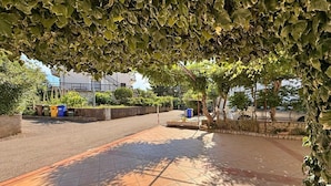 A paved outdoor area with tiled flooring, surrounded by greenery and a stone wall. - Apartment Dragica - sea view, 350 m from sea, balcony, free parking, BBQ (Šilo)
