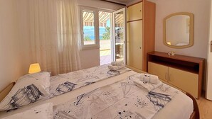 A bedroom with a bed, a bedside table, a mirror, and a view of the outdoors. - Apartment Dragica - sea view, 350 m from sea, balcony, free parking, BBQ (Šilo)