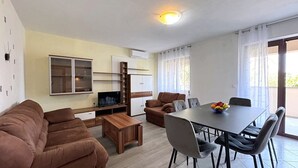 Una sala de estar moderna con sofá, televisor y zona de comedor con sillas y mesa.