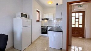 A compact kitchen with a white refrigerator, microwave, oven, and sink.