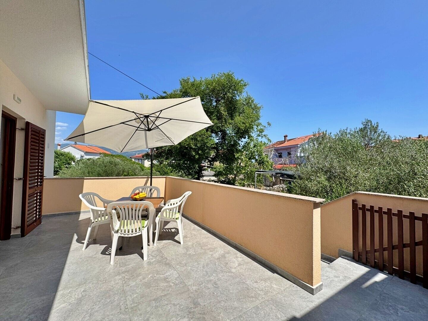 A balcony with a table and chairs, a large umbrella, and a view of the surrounding area.
