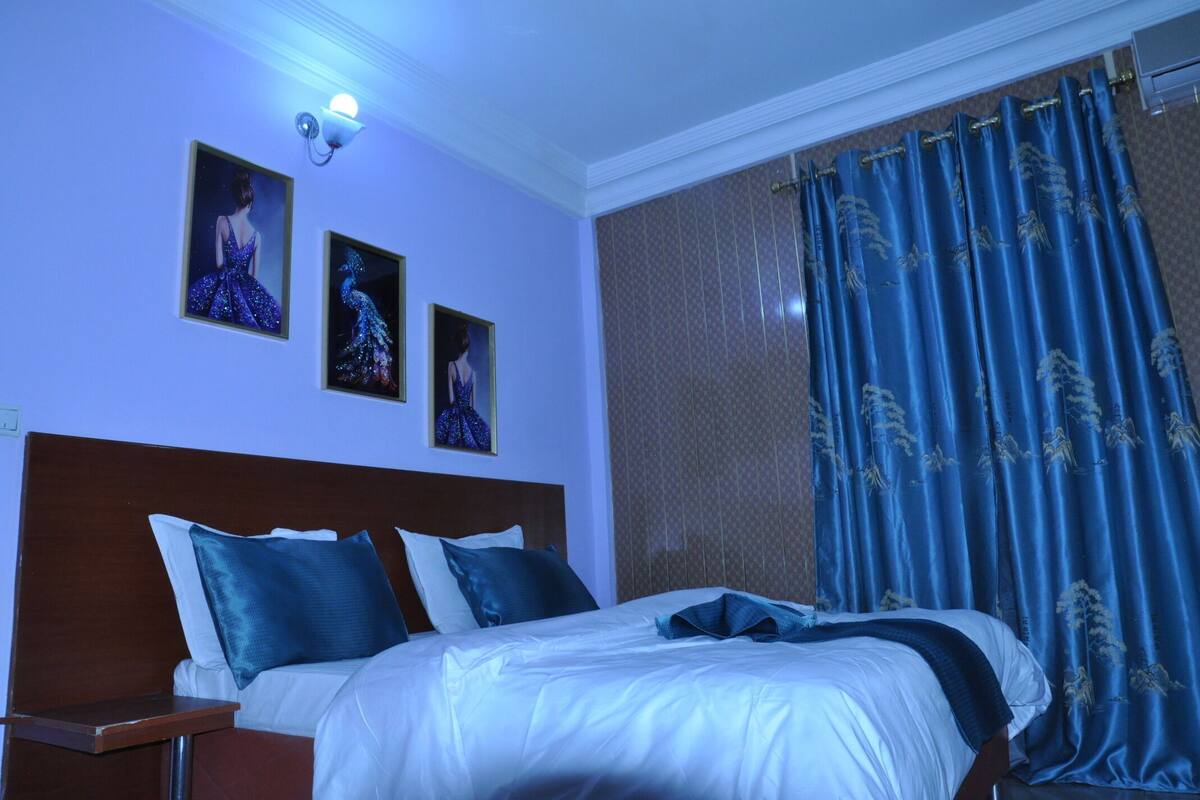 A hotel room with a bed, a nightstand, and a wall with three framed pictures.