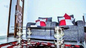 Un salon avec un canapé gris, des coussins rouges et blancs, une table basse en verre et un tapis à motifs rouges et noirs.