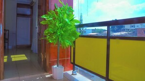 Un balcon orné d’un pot de fleurs, avec une rambarde jaune et une vue sur les bâtiments en arrière-plan.