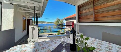 A balcony with a table set for two, overlooking a coastal view.