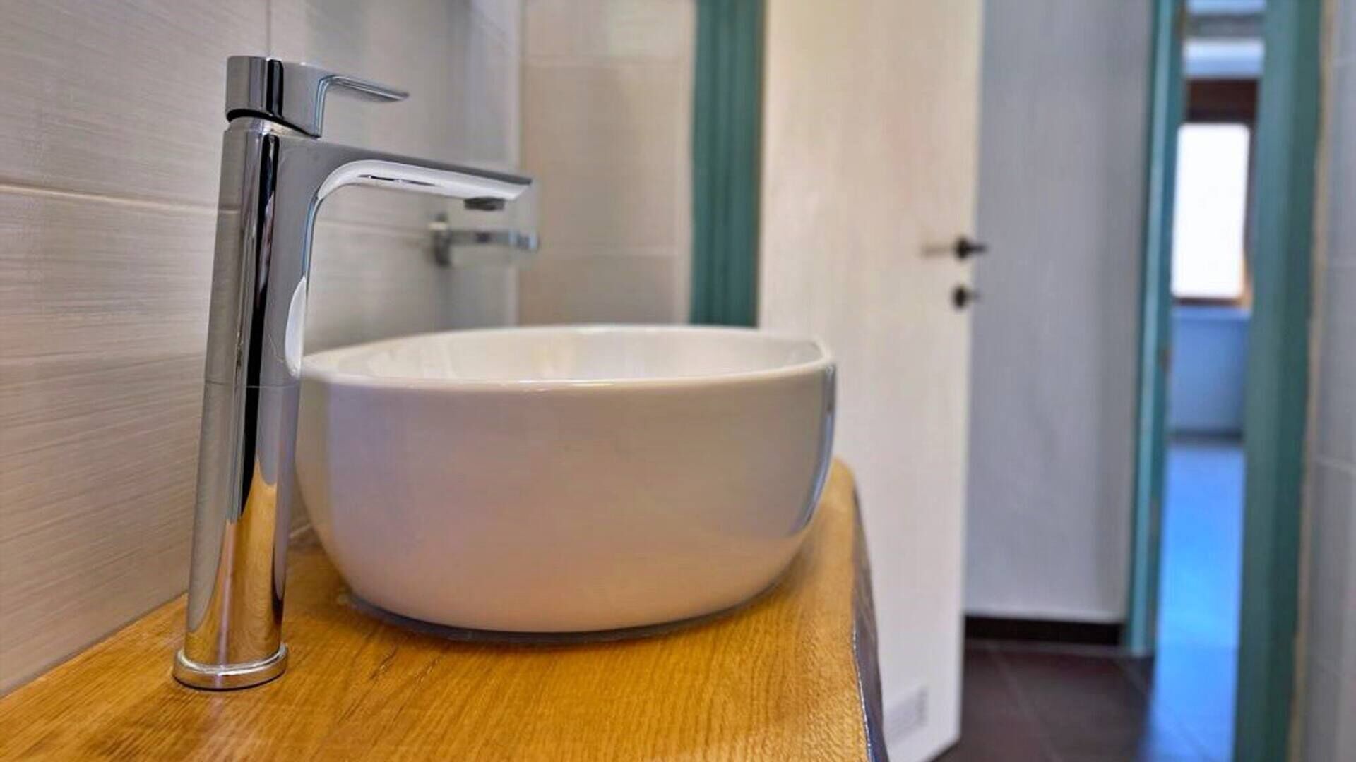 A modern bathroom with a white ceramic sink and a chrome faucet on a wooden countertop.