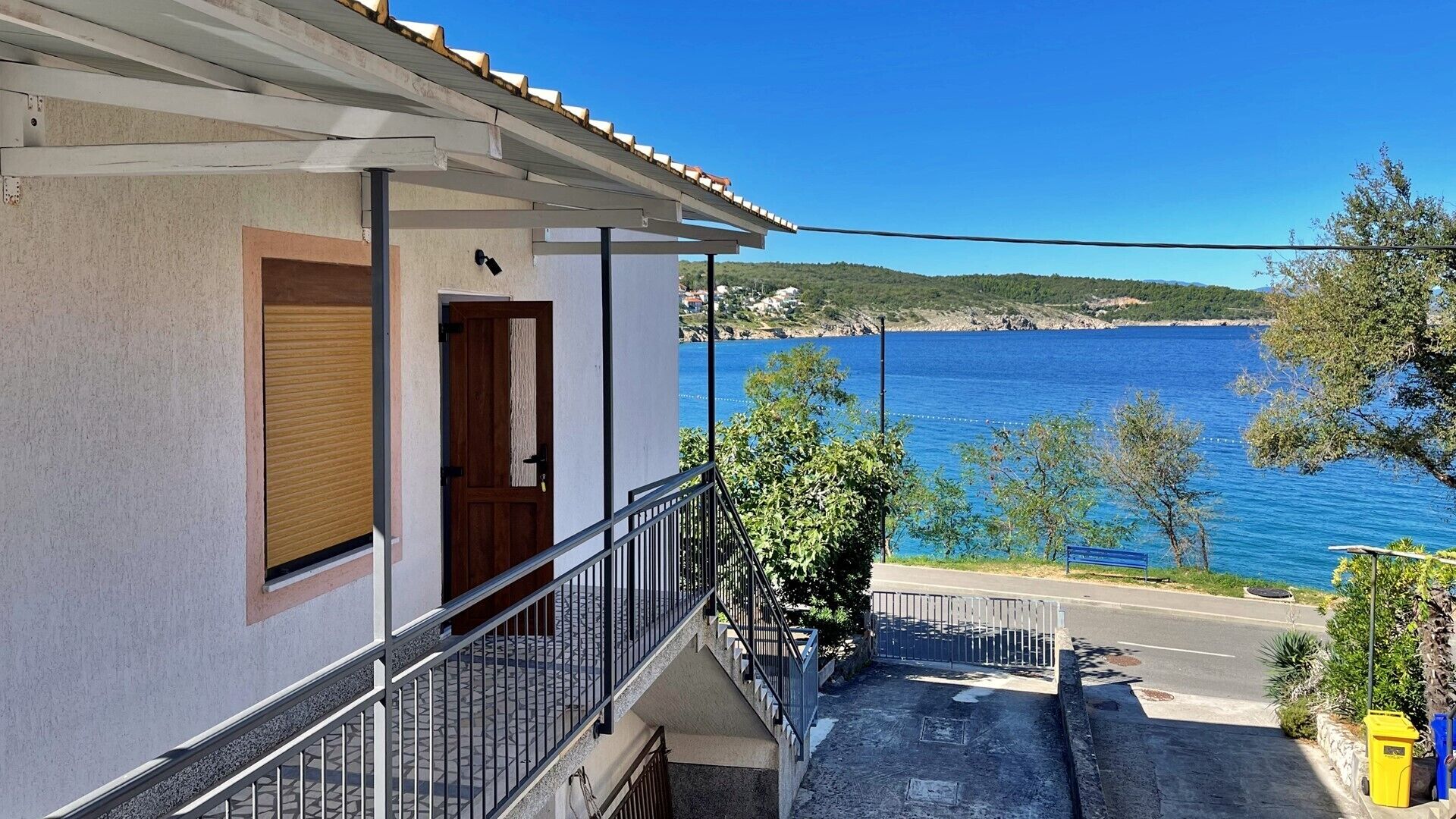 A building with a balcony overlooking a body of water, a clear sky, and a distant landscape.