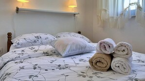 A neatly made bed with floral bedding, two bedside lamps, and rolled towels on the bed.