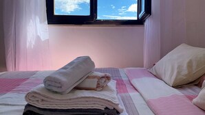 A neatly made bed with a pink and white checkered bedspread, a white pillow, and a stack of folded towels.